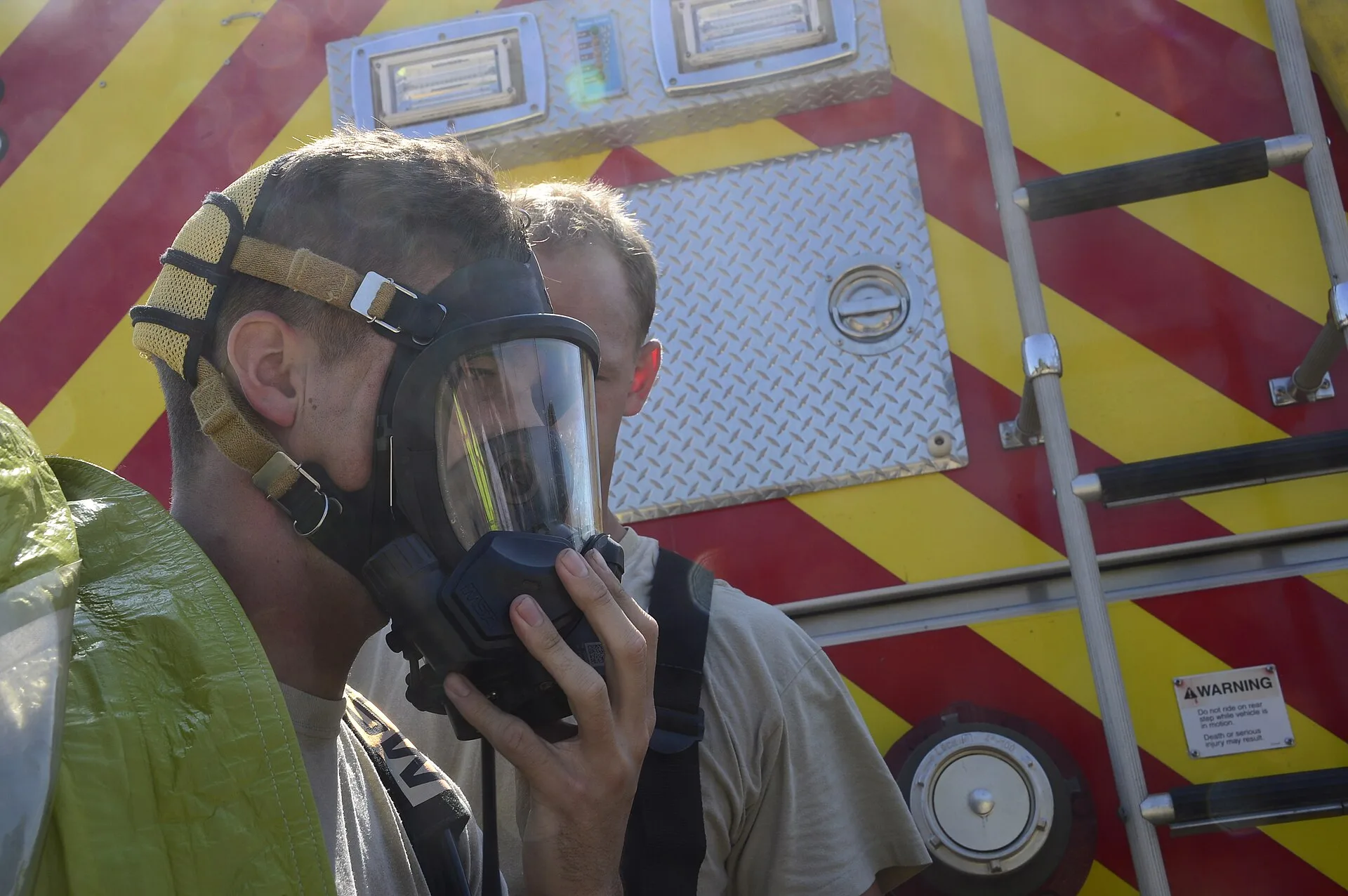 File photo: Two firefighters in protective suits, one helping the other adjust a respirator mask, in front of a fire truck during a hazardous materials training exercise. Representative image; does not show the Uxbridge exercise.